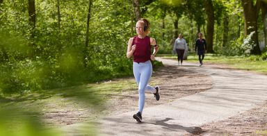 Girl running with her headset on in a park with green trees